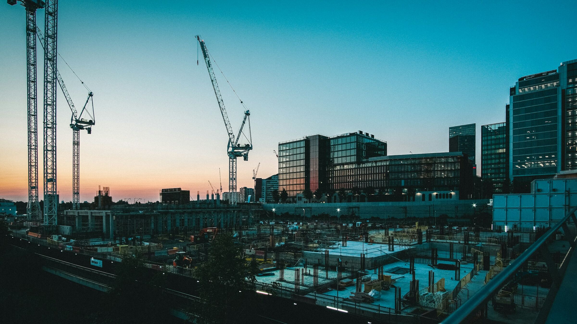 Tiga tower crane di atas galian konstruksi pada waktu senja, langit biru tua.